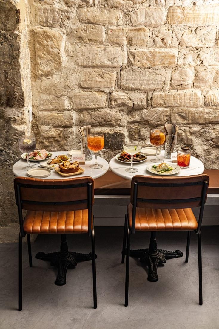 La salle en lumière de jour : tables en marbre, pierre et chaises en cuir cognac